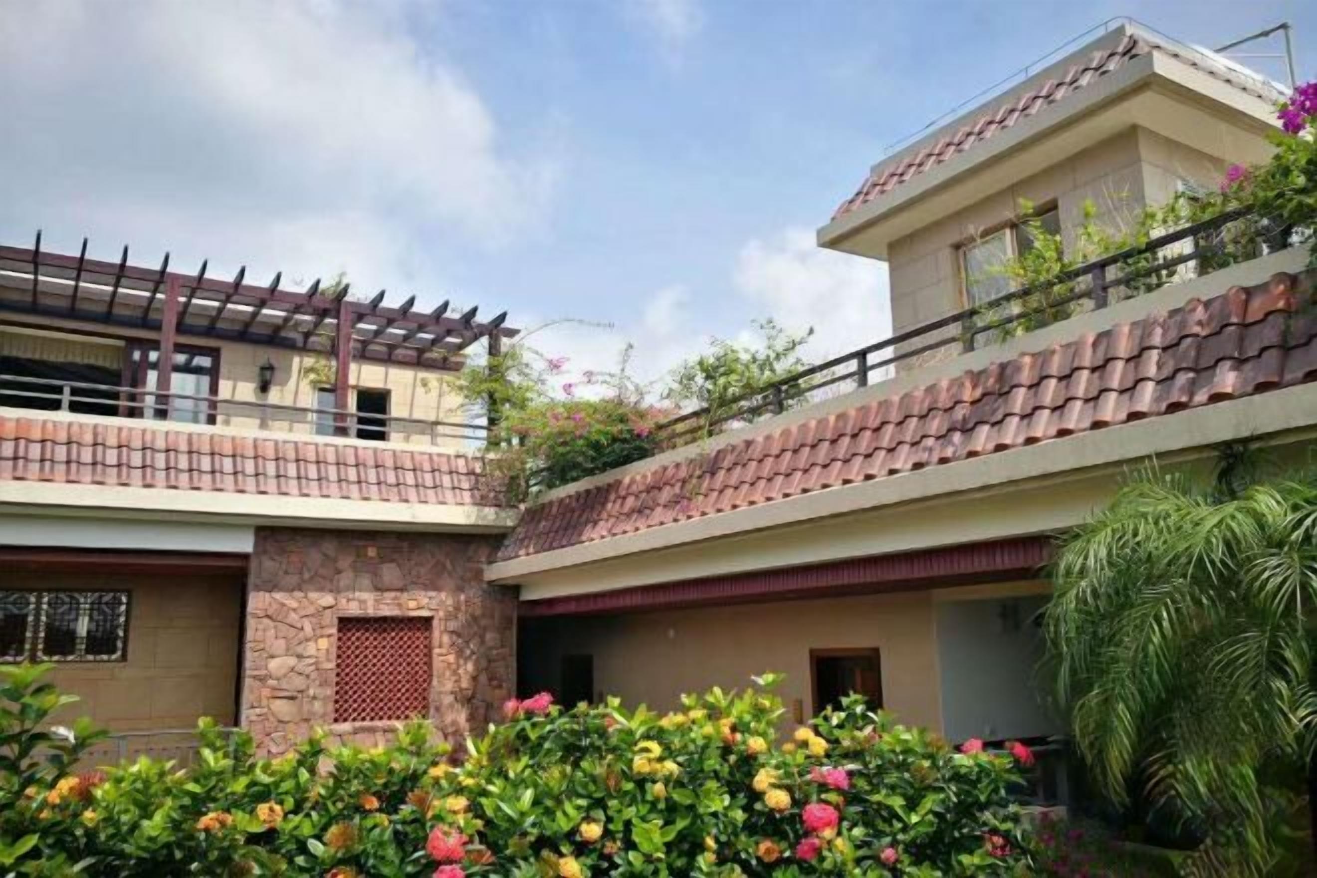 Un edificio residencial de dos pisos con un balcón, fachada de piedra y un jardín con plantas florecientes.