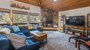 A cozy living room with a blue sofa, a fireplace, a TV, and a stone wall. - 6 Lynx Sunriver (Sunriver)