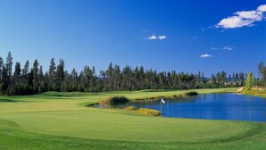 A golf course with a pond, surrounded by trees and a clear sky. - 6 Lynx Sunriver (Sunriver)