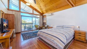 Een slaapkamer met een groot bed, een bureau met computer, een televisie en een balkon met stoelen.