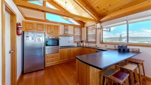 Een moderne keuken met houten kastjes, roestvrijstalen apparatuur en een groot raam met uitzicht op het landschap.
