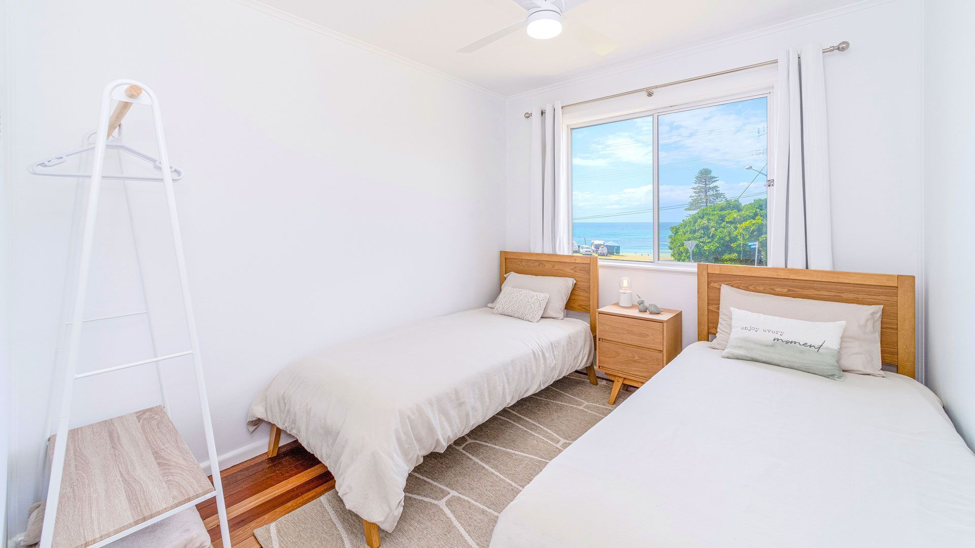 Ein Schlafzimmer mit zwei Einzelbetten, einem hölzernen Nachttisch, einem weißen Kleiderschrank und einem Fenster mit Meerblick.