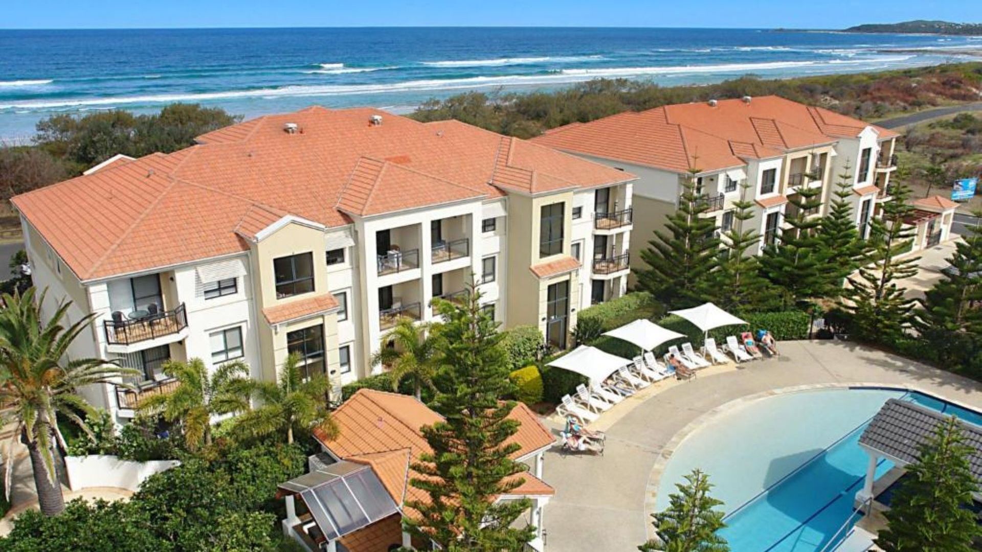 A beachfront hotel with multiple balconies, a pool, and a view of the ocean.