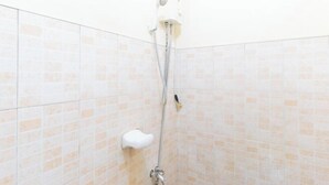 Suihkussa on käsisuihkupää ja seinään kiinnitetty hana, ja taustalla on laatoitettu seinä, jossa on vaalean beigen sävyinen kuvio.