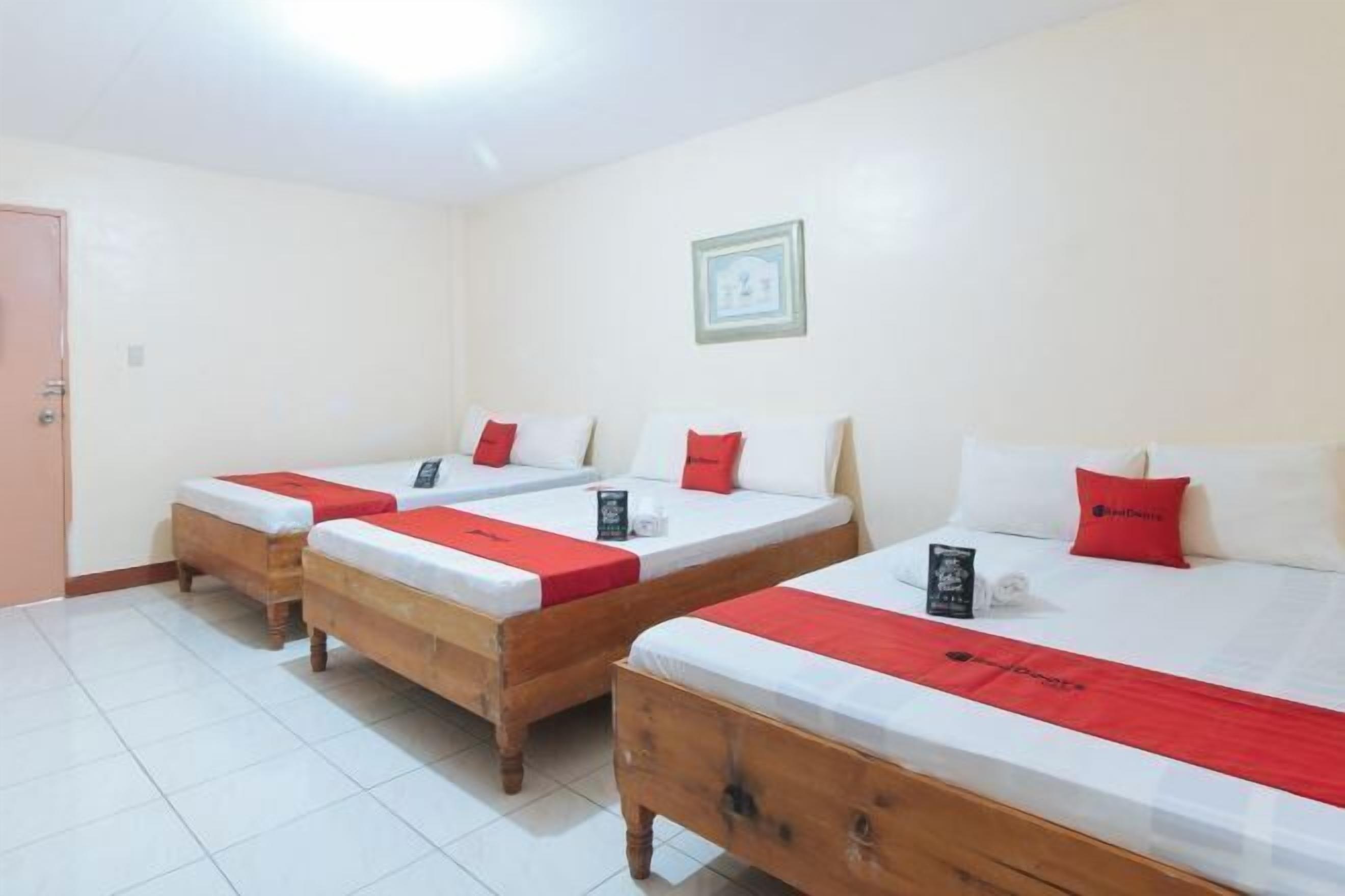 A hotel room with three wooden beds, each with white bedding and red accents.