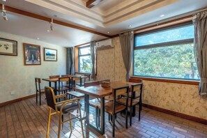 A dining area with wooden tables and chairs, large windows with curtains, and framed pictures on the walls. - the Four Seasons the Inn (Lijiang)