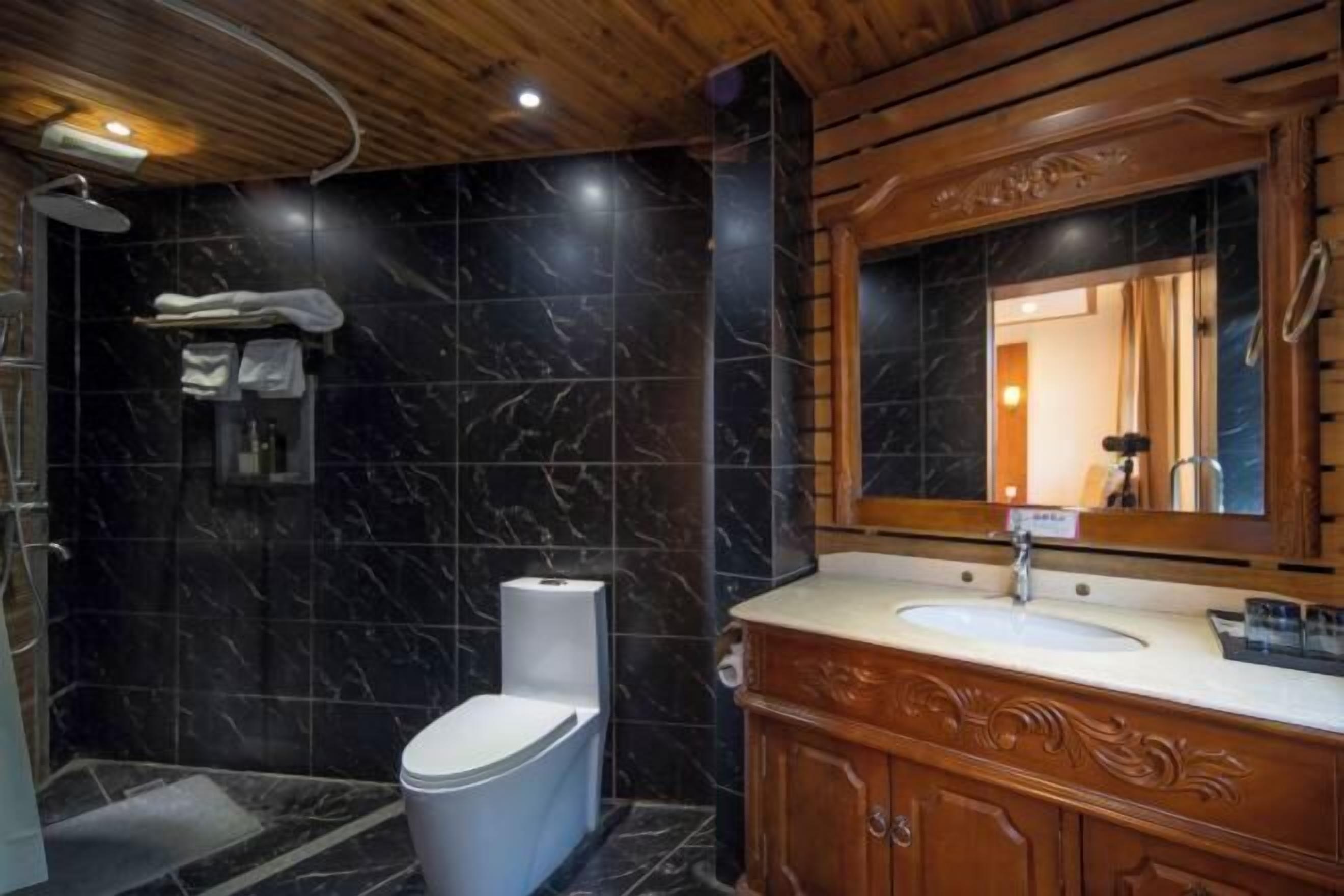 A bathroom with a marble wall, a wooden vanity, a toilet, and a shower area.