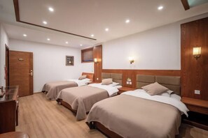 Ein Hotelzimmer mit drei Betten, Holz-Kopfteilen und einem Schreibtisch mit Stuhl.