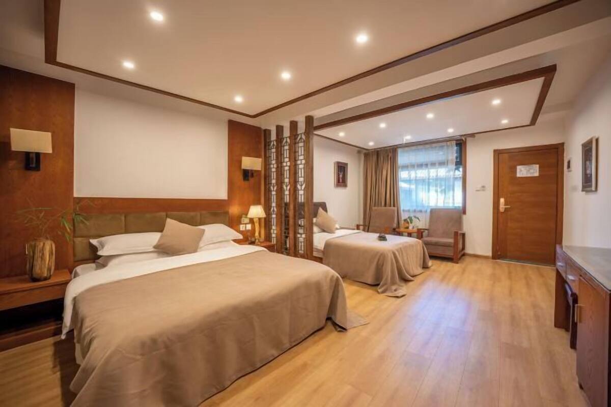 A hotel room with two beds, a wooden floor, a desk, and a window with curtains.