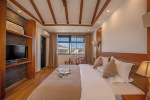 Ein Hotelzimmer mit einem großen Bett, einem Flachbildfernseher, einem kleinen Tisch und einem Fenster mit Blick.