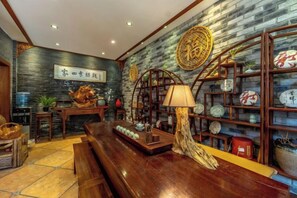 Un intérieur traditionnel avec une table en bois, des étagères ornées d’objets décoratifs et un mur décoré de calligraphies.