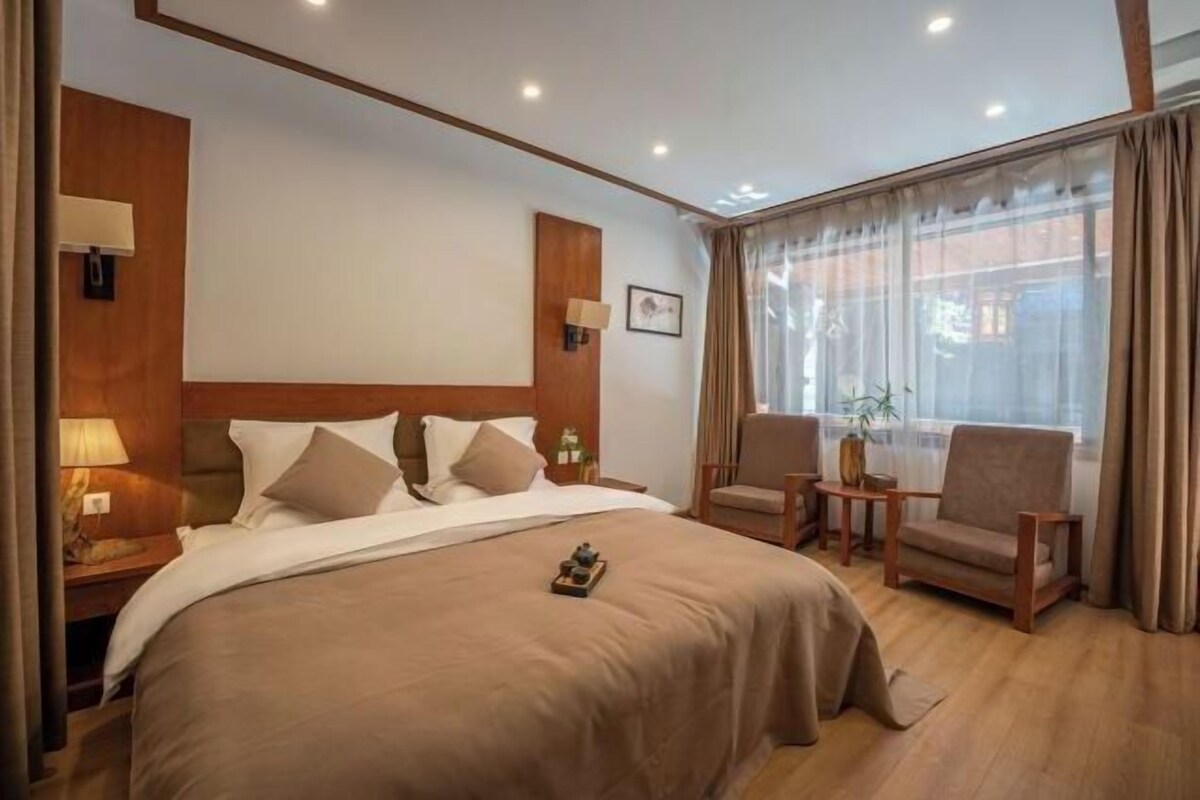 Ein Hotelzimmer mit einem großen Bett, zwei Sesseln, einem kleinen Tisch und einem Fenster mit Vorhängen.