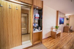 Una habitación de hotel moderna con un armario de madera, una kitchenette pequeña con hervidor, un televisor de pantalla plana y una mesita con una planta.