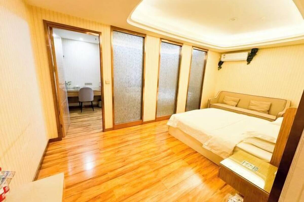 A bedroom with a wooden floor, a bed, a small table, and a sliding door leading to a bathroom.