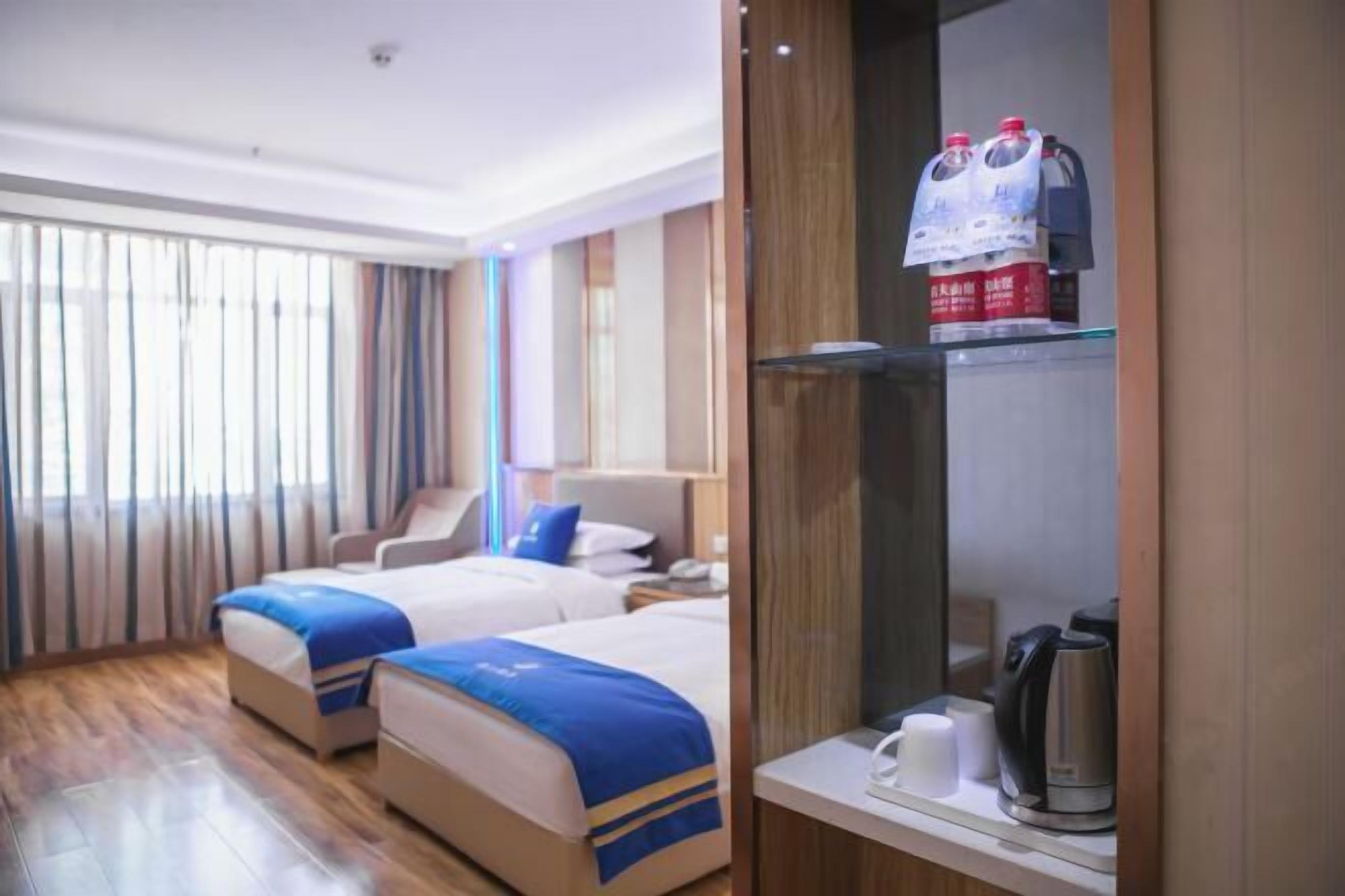 Habitación de hotel con dos camas, cafetera y un estante con agua embotellada.