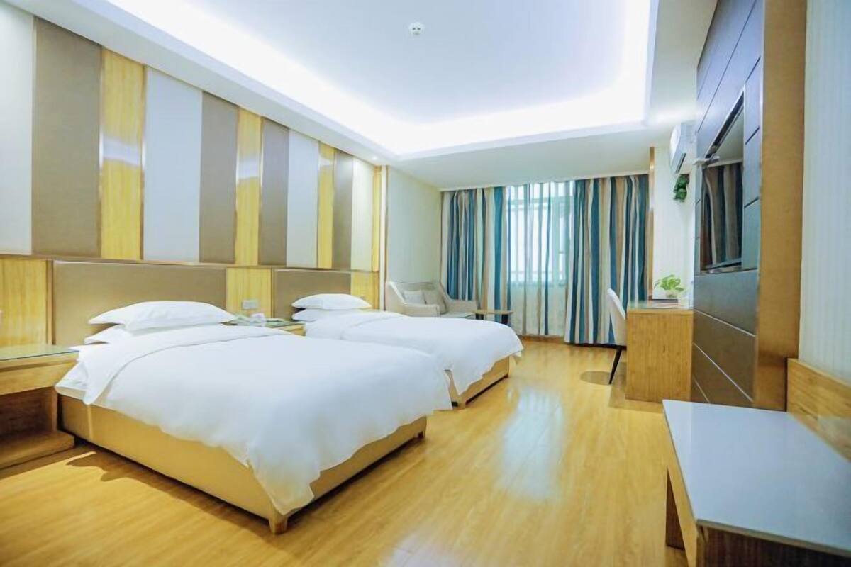 A hotel room with two beds, a desk, a chair, and a TV.