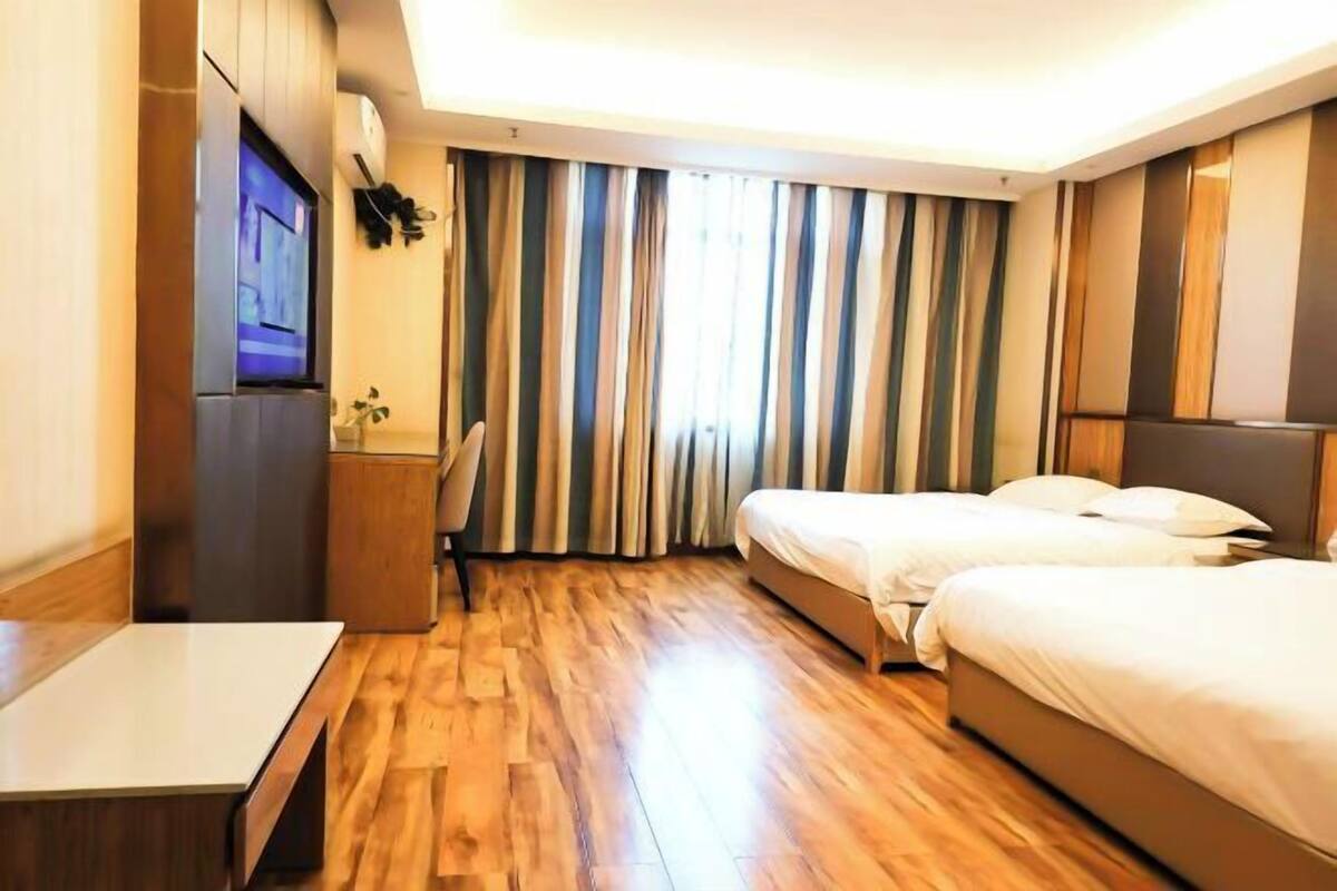 A hotel room with a wooden floor, two beds, a desk, a TV, and striped curtains.