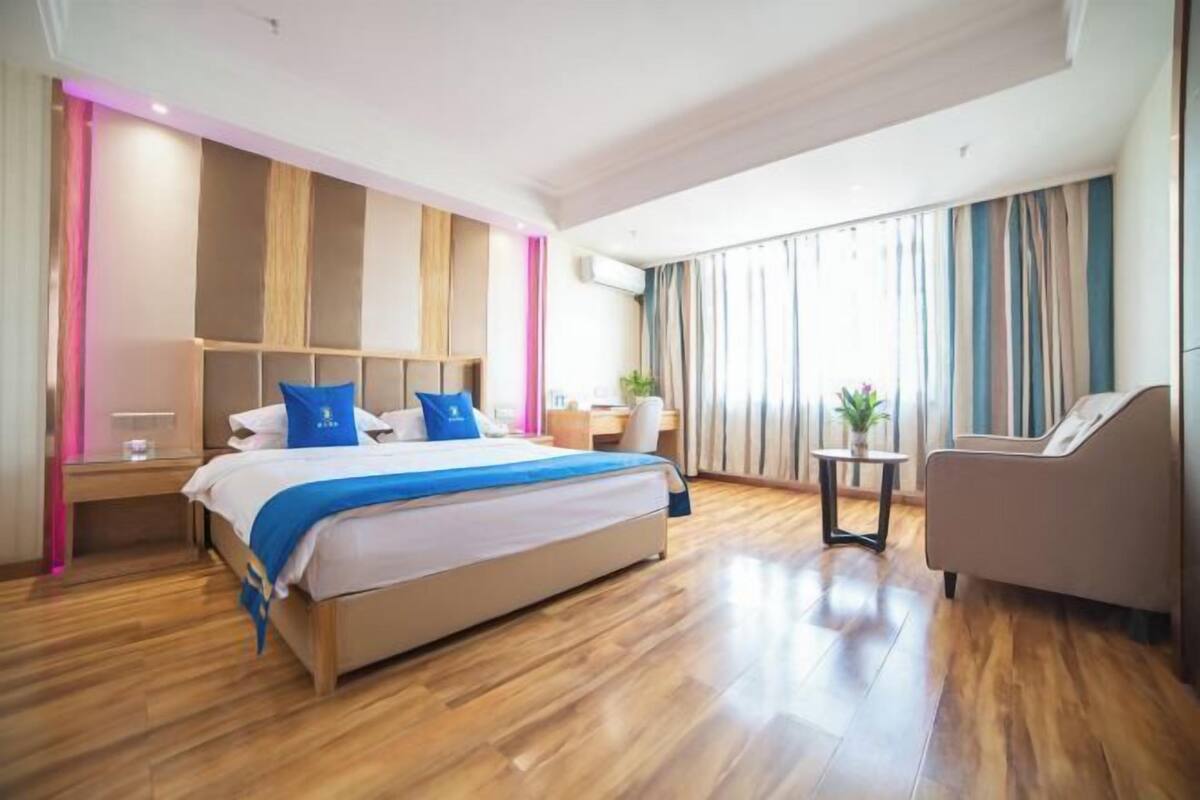 A modern hotel room with a large bed, a desk, a chair, and a view of the city.