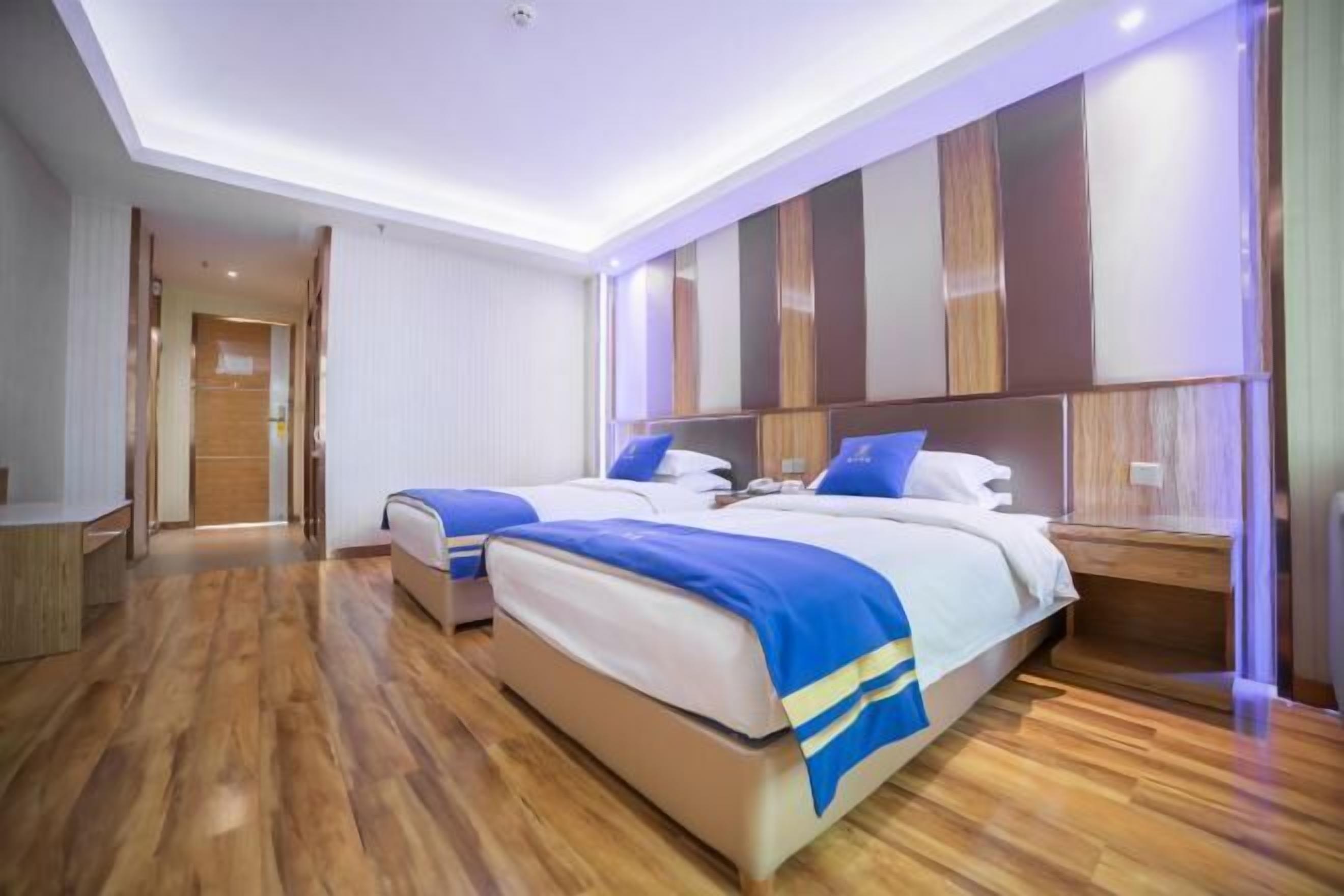 Ein modernes Hotelzimmer mit zwei Betten, Holzboden und einer großen Wandanlage mit Stauraum.
