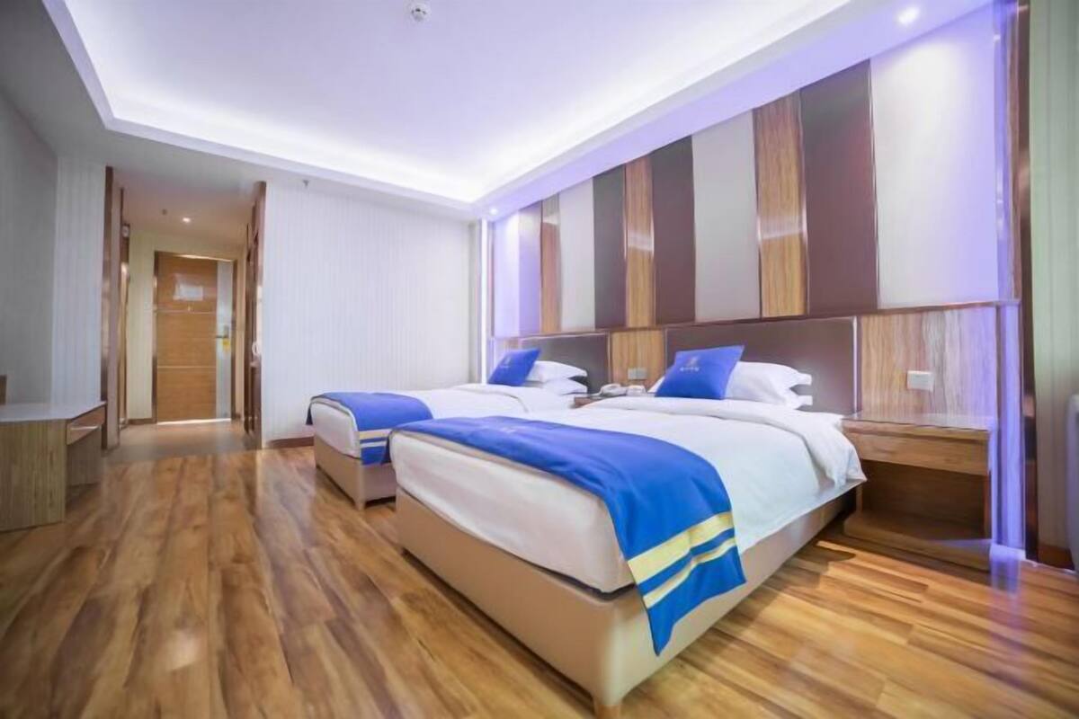 A modern hotel room with two beds, wooden flooring, and a large wall unit with storage.