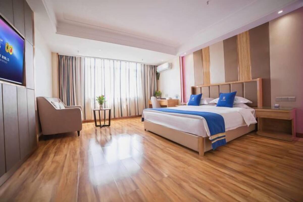 A modern hotel room with a large bed, a TV, a desk, and a small table with a plant.