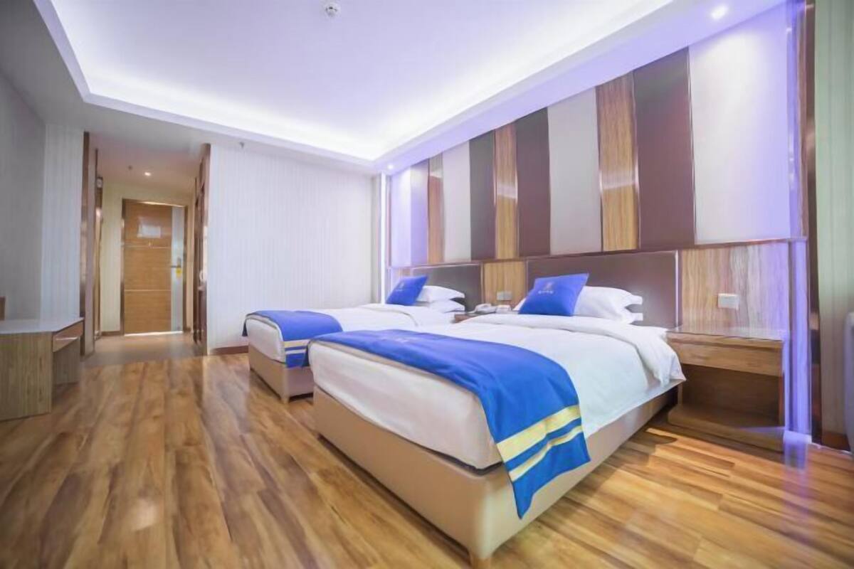 A hotel room with two beds, wooden flooring, a modern wall design, and a visible door leading to another room.