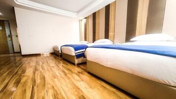 A hotel room with two beds, wooden flooring, and a modern design.