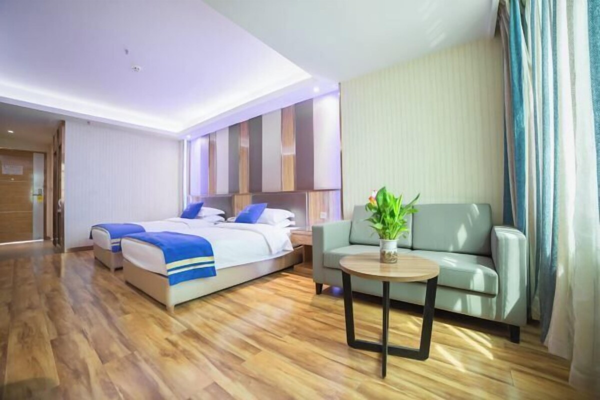 Habitación de hotel con cama doble, sofá, una mesita con planta y suelo de madera.