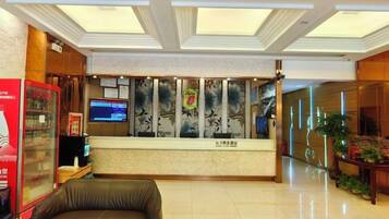 A hotel reception area with a reception desk, a television, a refrigerator, and a seating area.