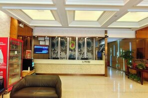 Zona de recepción de un hotel con mostrador, televisor, refrigerador y asientos.