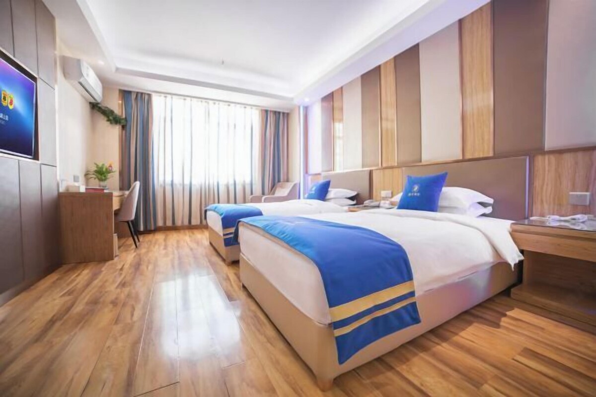 Habitación de hotel con dos camas, piso de madera, televisión y ventana con cortinas.