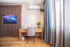 Habitación de hotel con escritorio de madera, una silla, televisor fijado a la pared, cubo de basura y ventana con cortinas.