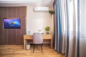 Habitación de hotel con escritorio de madera, una silla, televisor fijado a la pared, cubo de basura y ventana con cortinas.