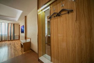 Una habitación de hotel moderna con un armario de madera, una mesa con superficie de vidrio y un espejo grande.