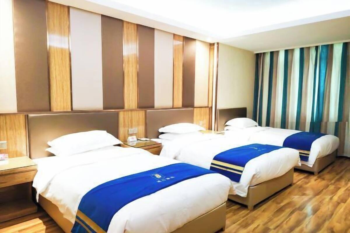 A hotel room with three beds, wooden paneling on the walls, and a striped curtain.