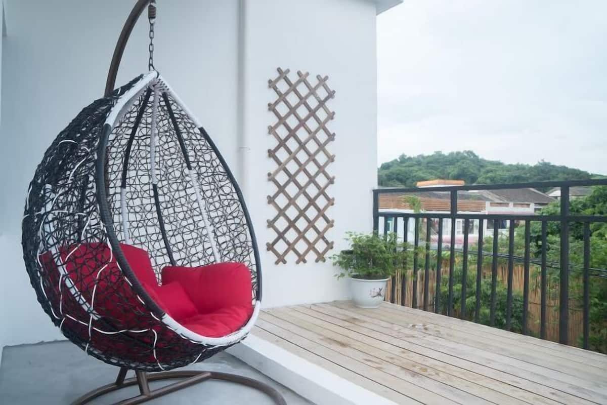 A hanging chair with a red cushion on a balcony with a wooden floor and a lattice wall.