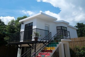 A two-story building with a balcony, a staircase with colorful steps, and a wooden fence in the background.