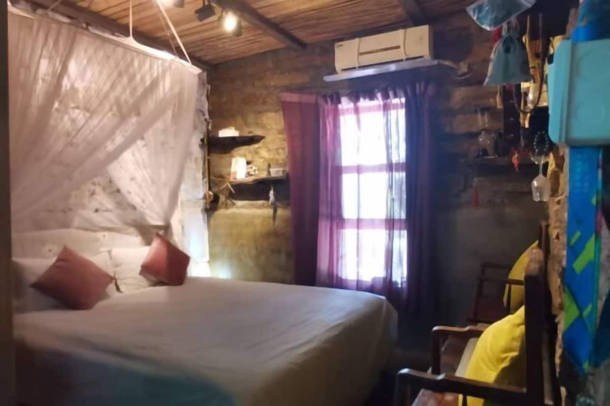 A rustic room with a bed, a chair, and a window with curtains.