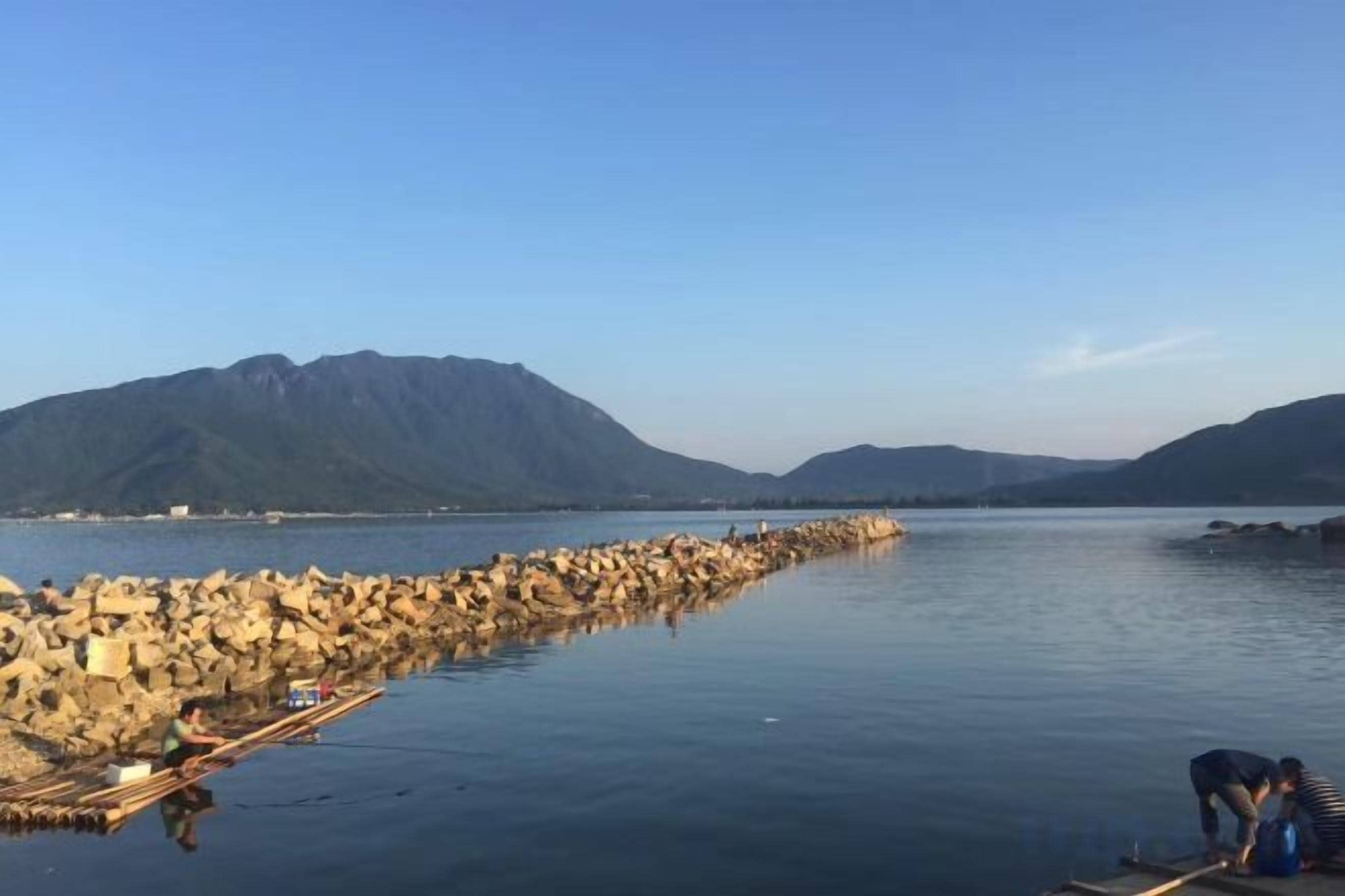 A calm lake with a rocky shoreline and mountains in the background.
