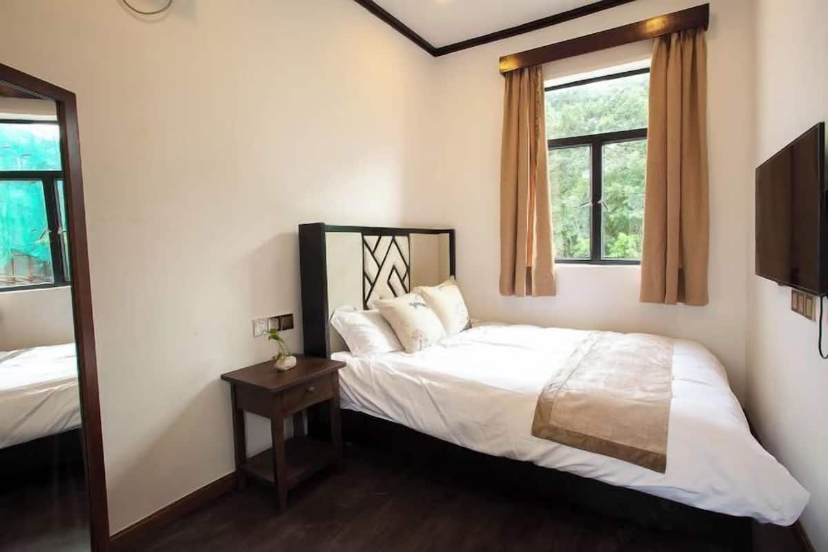 A bedroom with a bed, a nightstand, a mirror, a window with curtains, and a TV mounted on the wall.