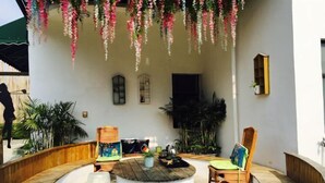 Un espacio al aire libre cubierto con una mesa redonda, dos sillas y decoración floral colgante.