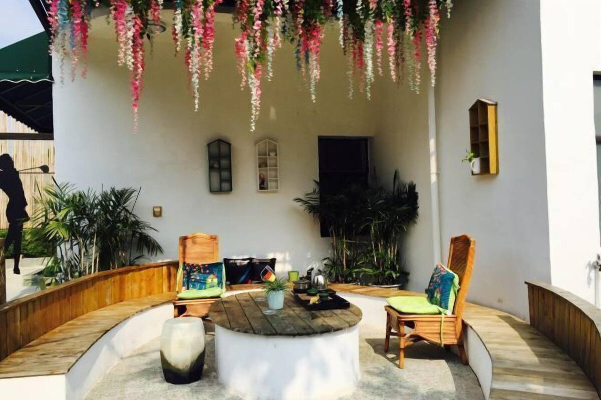 A covered outdoor seating area with a round table, two chairs, and hanging floral decorations.