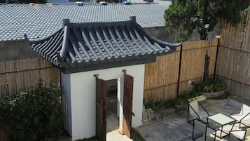 A small traditional Japanese-style building with a tiled roof, a wooden door, and a small patio area with a table and chairs.