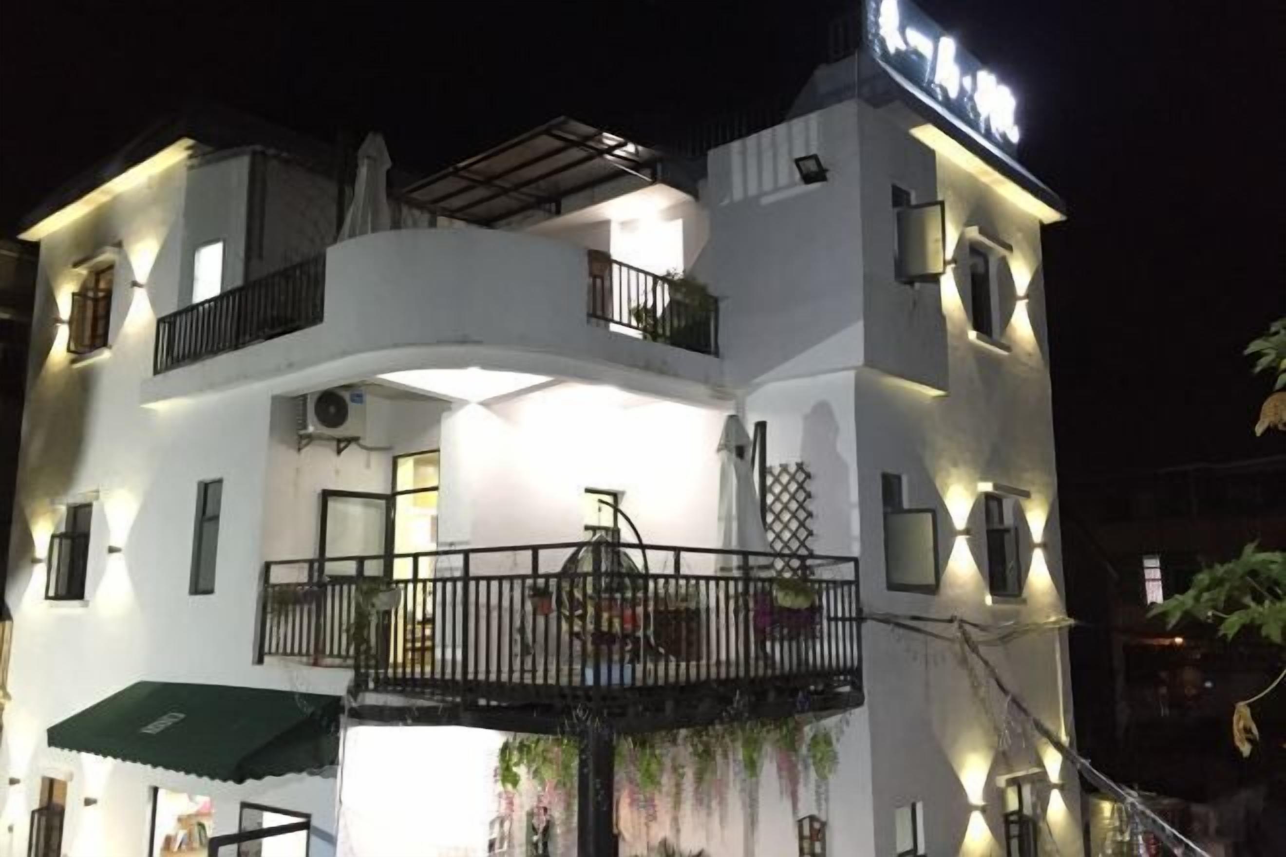 A multi-story hotel with a balcony on the second floor, a covered outdoor seating area, and a sign indicating the name of the establishment.