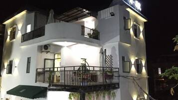 A multi-story hotel with a balcony on the second floor, a covered outdoor seating area, and a sign indicating the name of the establishment.