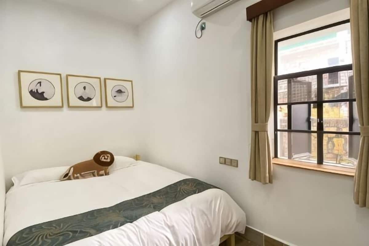 A bedroom with a bed, a window with curtains, and three framed pictures on the wall.