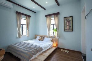 A bedroom with a bed, two windows with curtains, a bedside table with a lamp, and a wall-mounted artwork. - One More Homestay (Shenzhen)