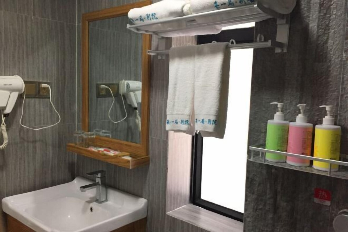 Un baño con un lavamanos blanco, un espejo, un perchero para toallas y una ventana.