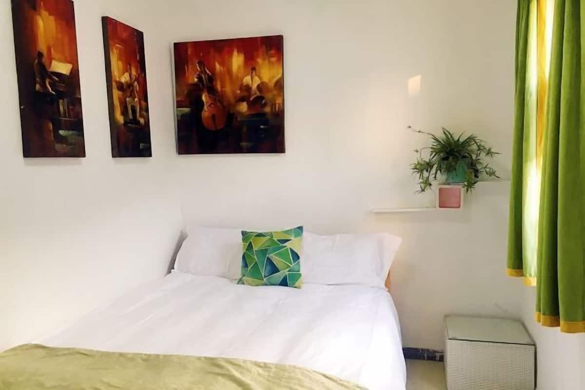 A hotel room with a bed, a wall-mounted air conditioner, and three paintings above the bed.