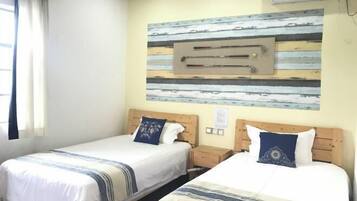 A hotel room with two beds, a wooden headboard, a wall-mounted air conditioning unit, and a window with curtains.